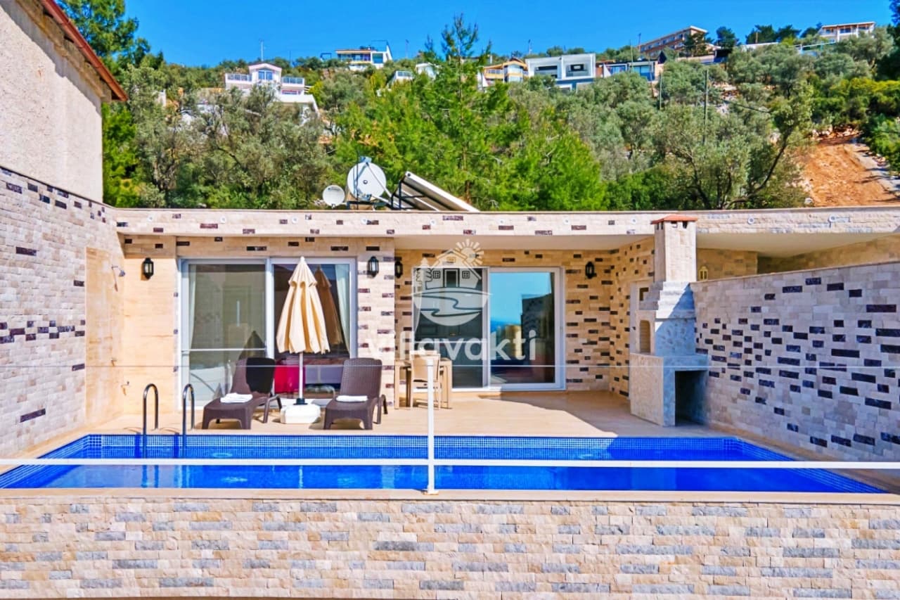 Taş duvarlı, barbekülü, özel havuzlu ve şezlonglu villa terası ile arka planda yamaçtaki evler.