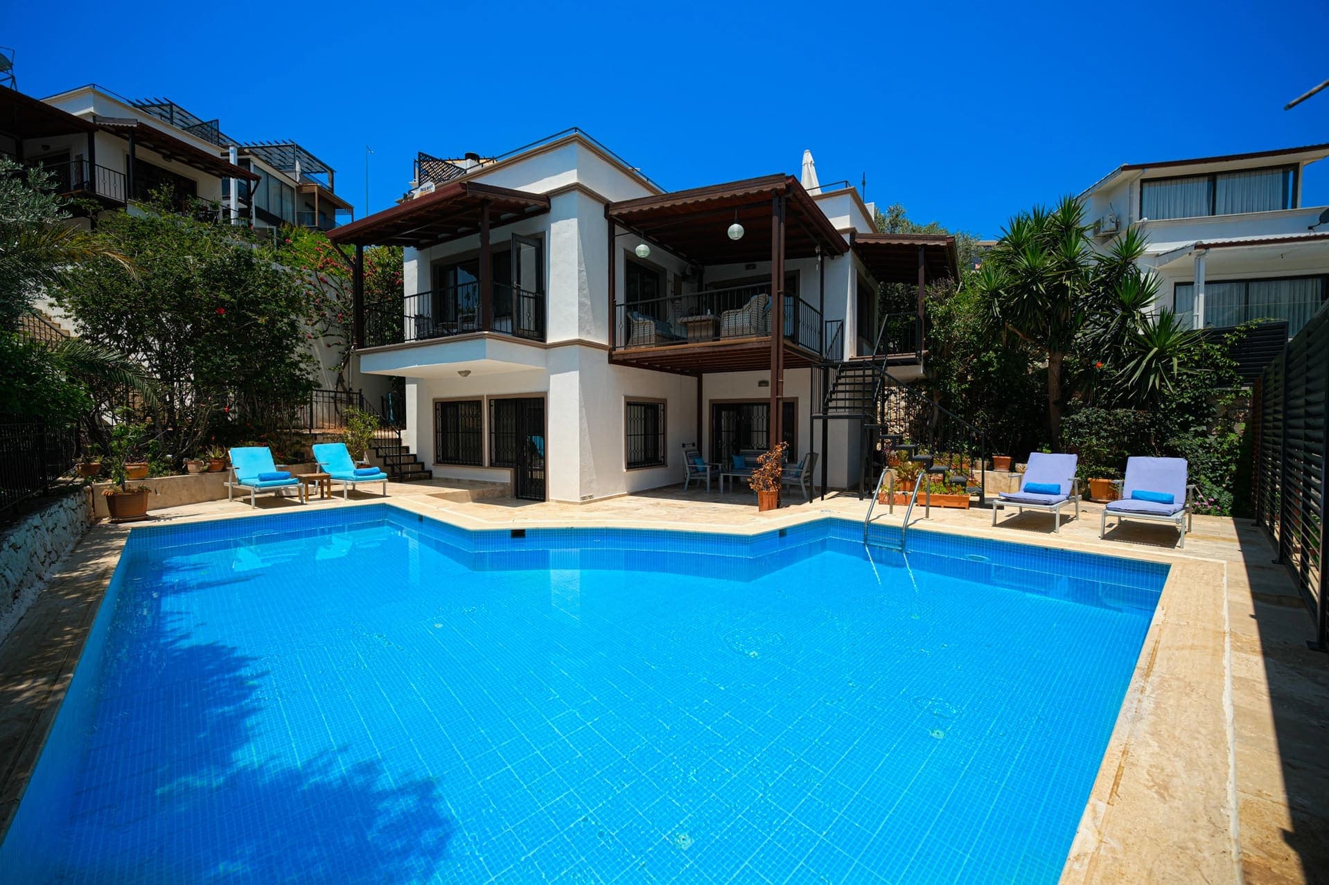 Önünde mavi fayanslı yüzme havuzu ve şezlonglar bulunan beyaz dış cepheli villa.