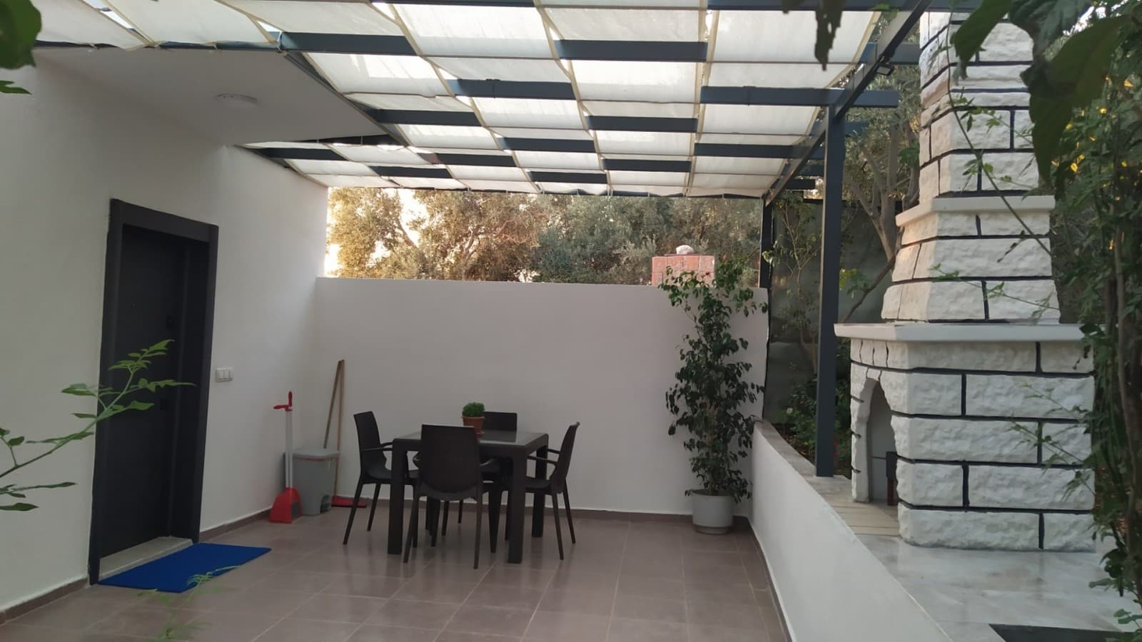 Üstü tenteyle kapatılmış, yemek masası ve taş şömine bulunan teras.