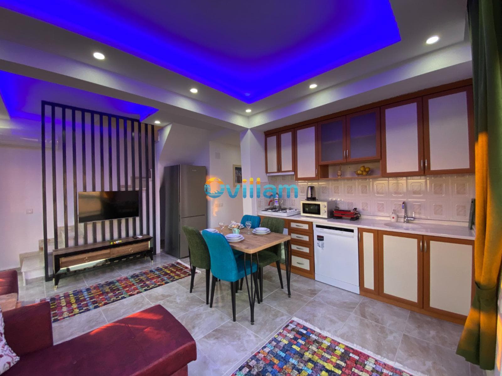 Mavi led aydınlatmalı tavanı olan, ahşap dolaplı mutfak ve yemek masası içeren salon.
