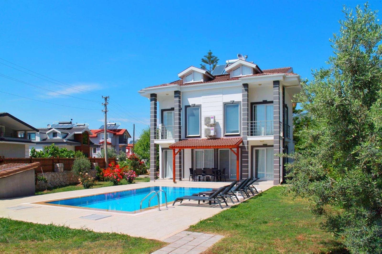 Gündüz vakti bahçesinde havuz ve şezlonglar bulunan iki katlı villa dış cephesi.