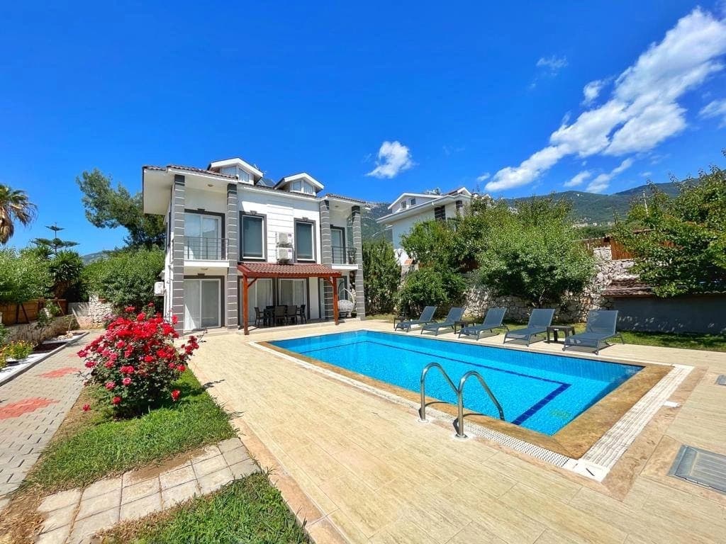Güneşli havada bahçesinde havuz ve şezlonglar bulunan iki katlı villa dış cephesi.