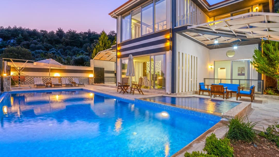 Akşam vakti aydınlatılmış havuzu ve şezlongları bulunan iki katlı villa.