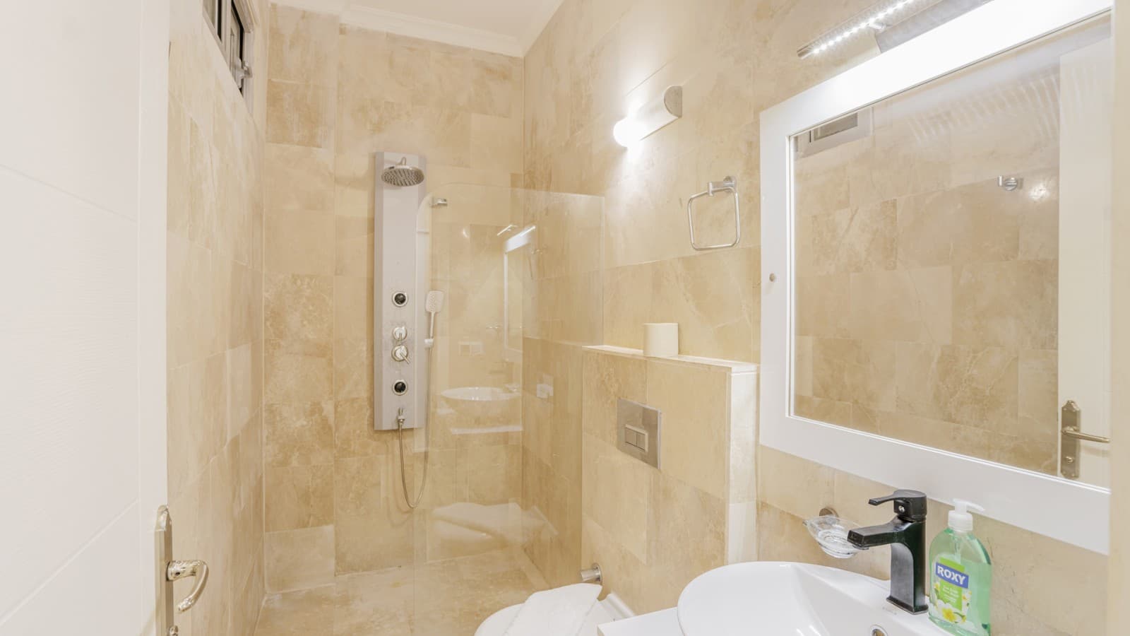 Bej tonlarında mermer kaplı banyoda cam duşakabin ve aynalı lavabo yer alıyor.