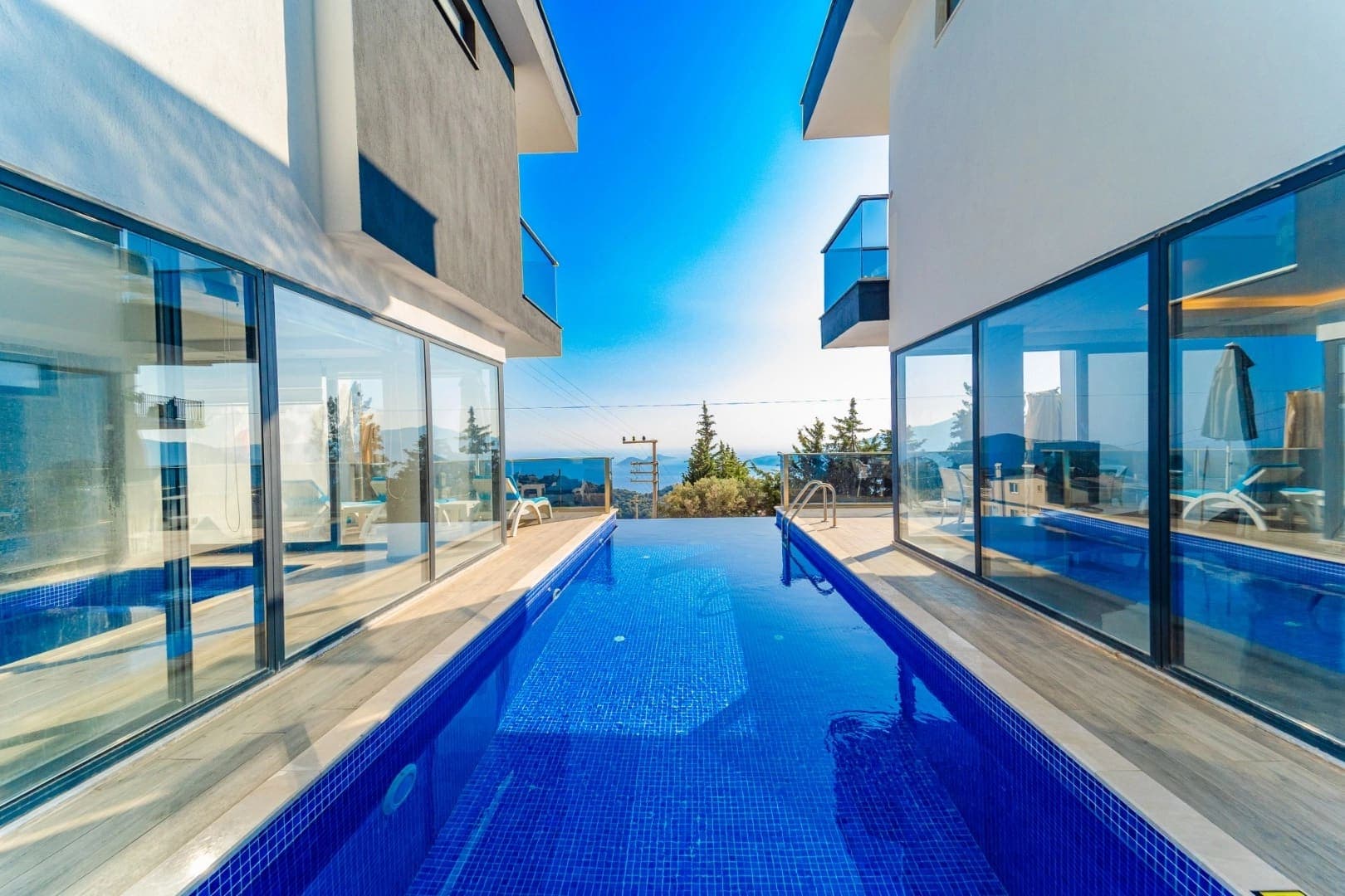 İki yapı arasında uzanan dikdörtgen yüzme havuzu ve cam cepheli modern villalar.