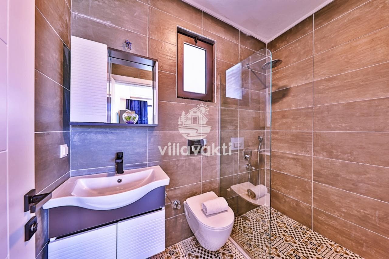 Kahverengi fayanslı, cam duşakabinli ve modern lavabolu banyo.