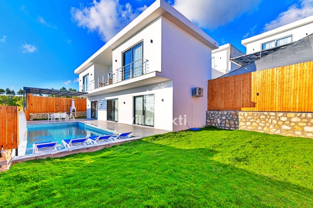 Geniş çim bahçeli, havuzlu ve iki katlı modern beyaz villa dış cephesi.