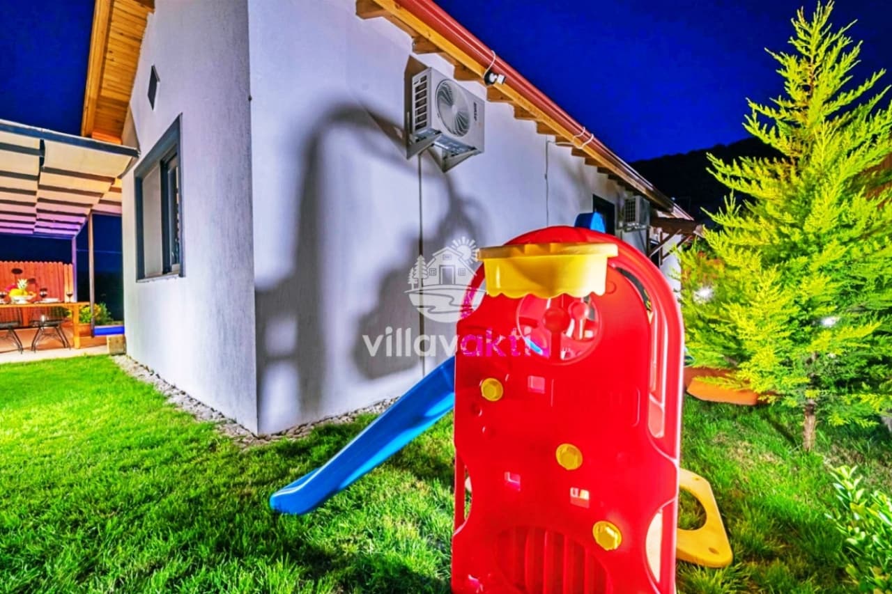 Gece aydınlatmalı villa bahçesindeki çim alanda plastik çocuk kaydırağı.