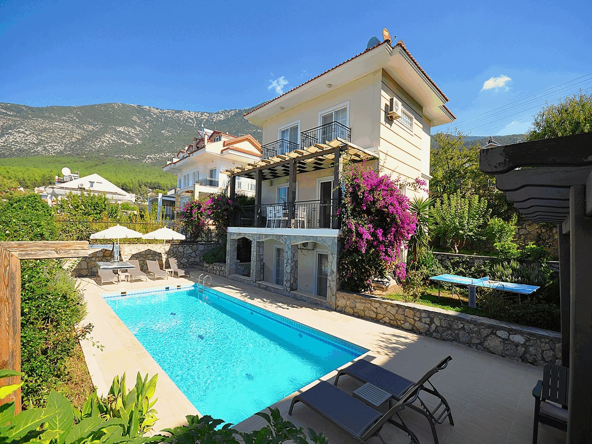 Güneşlenme alanına ve şezlonglara sahip özel yüzme havuzu ile bahçe içindeki iki katlı müstakil villa.