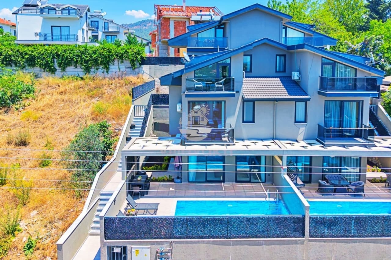 Çok katlı modern villanın dış cephesi ve önündeki havuzun havadan görünümü.