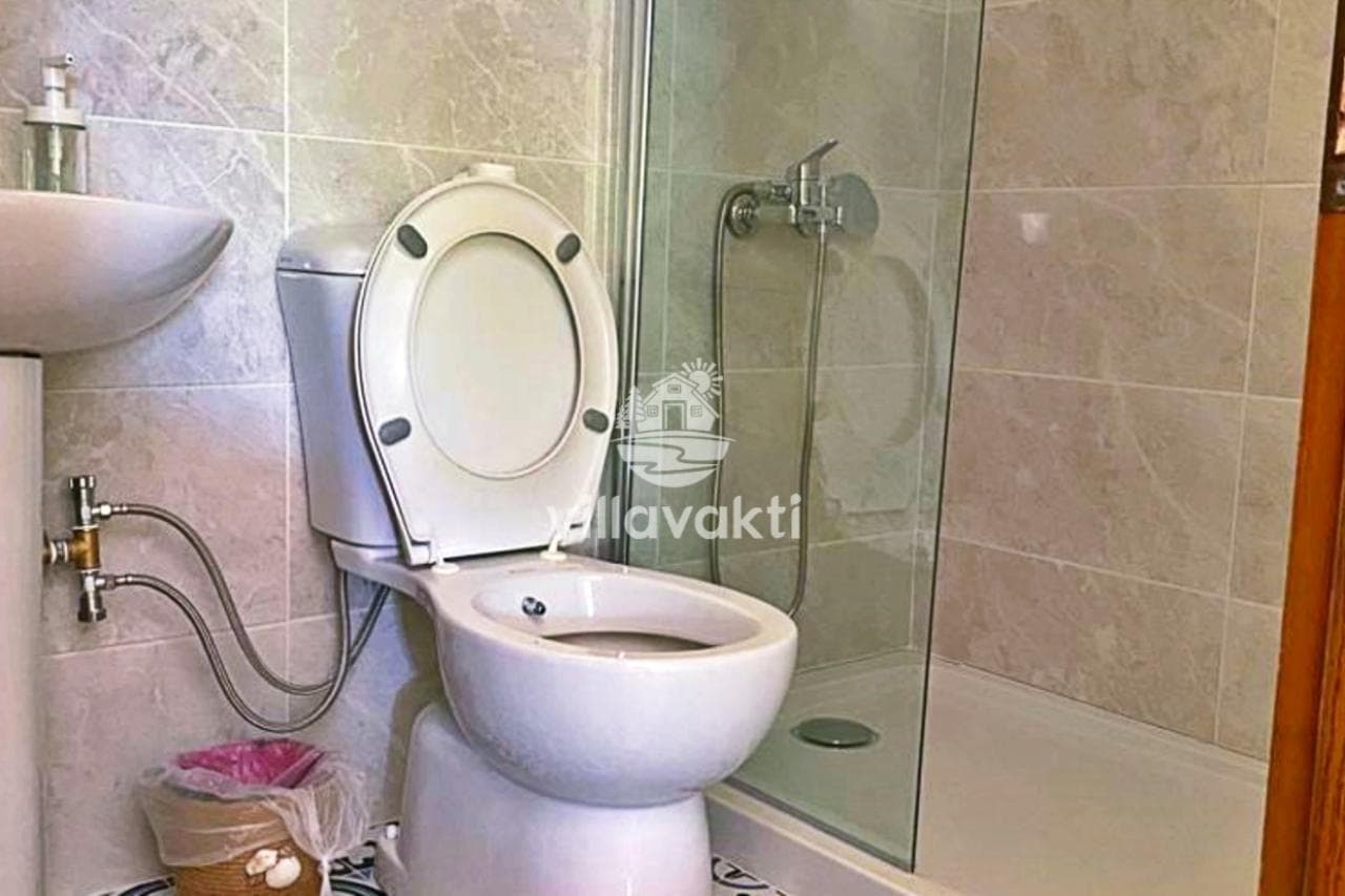 Bej seramik kaplı banyoda klozet, lavabo ve cam duş kabini bulunuyor.