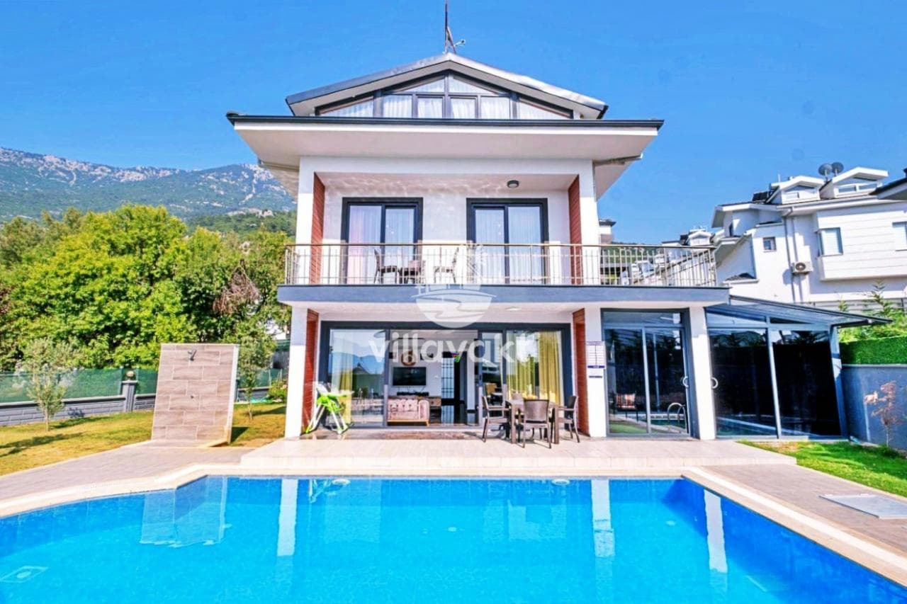 Önünde yüzme havuzu bulunan beyaz villa ve balkonundaki masa sandalyeler.