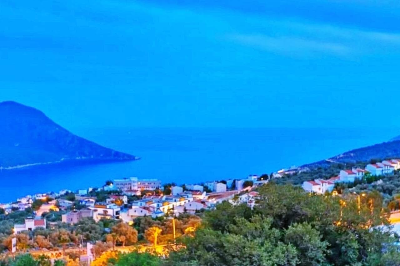 Alacakaranlıkta deniz, dağlar ve yerleşim yeri manzarası.