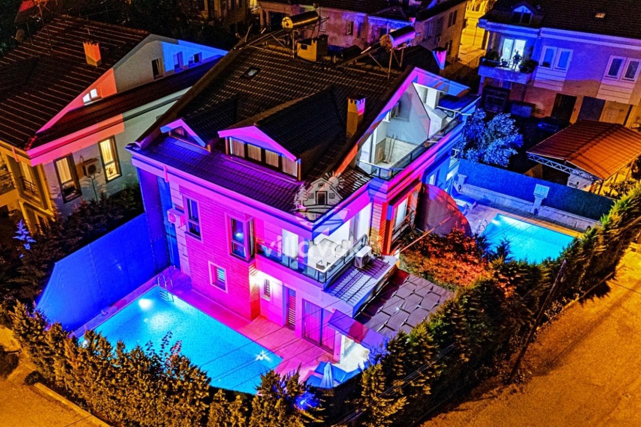Gece havuz aydınlatmalı, bahçeli ve çok katlı villanın havadan görünümü.
