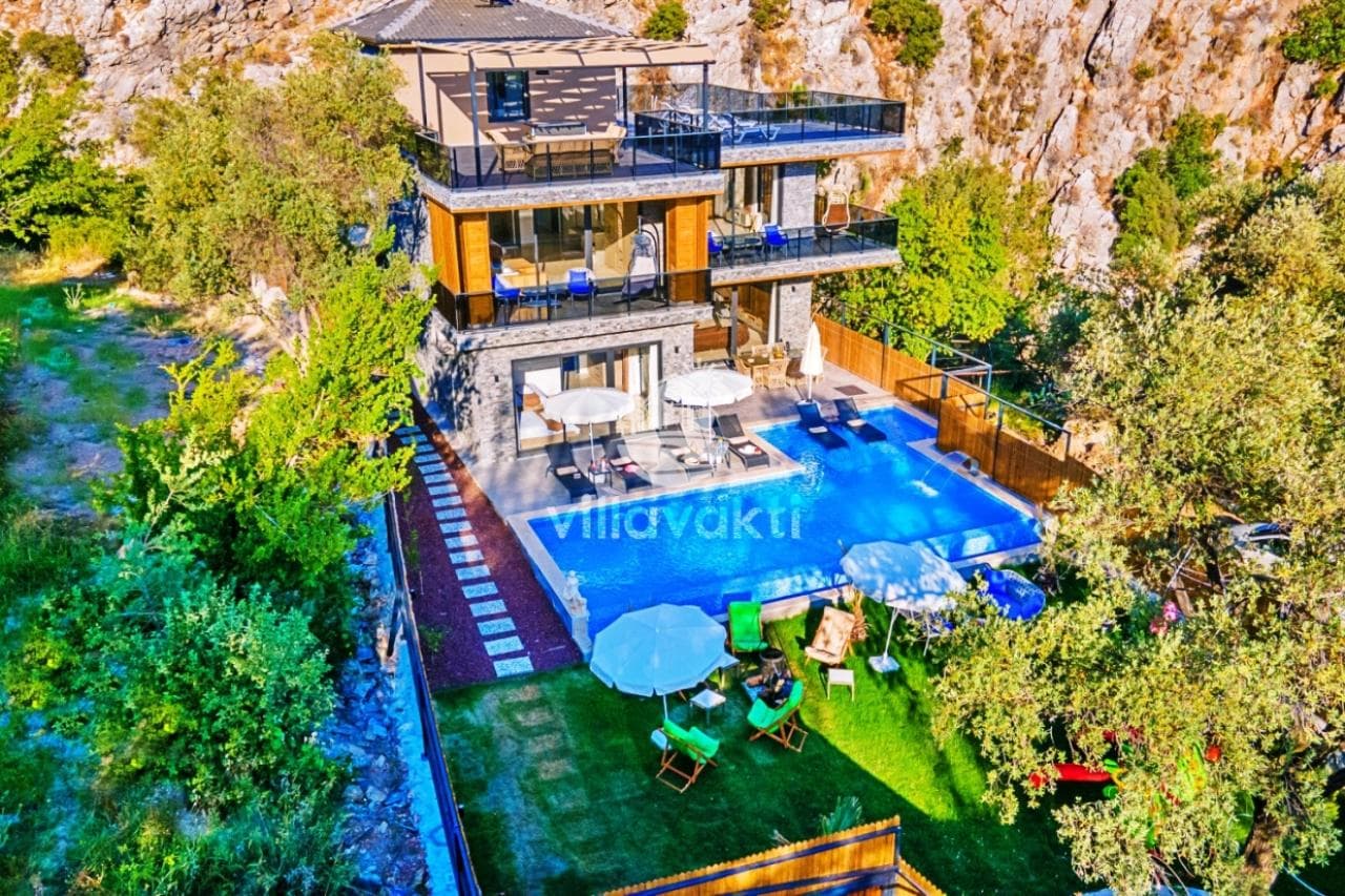 Dağ yamacında teraslı, çok katlı villa ve önündeki şezlonglu havuz.