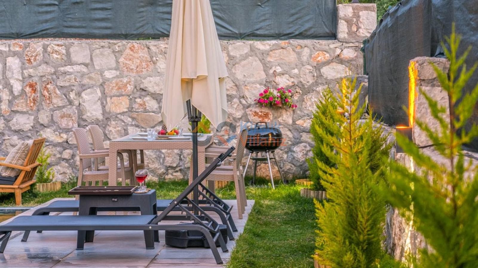 Yeşil çimler üzerinde yemek masası ve şezlong bulunan villa bahçesi.