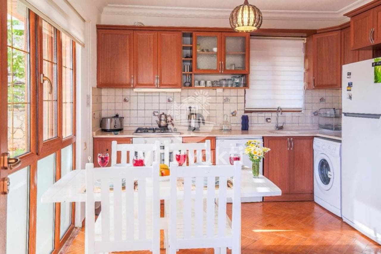 Ahşap dolaplı mutfakta beyaz yemek masası ve buzdolabı var.