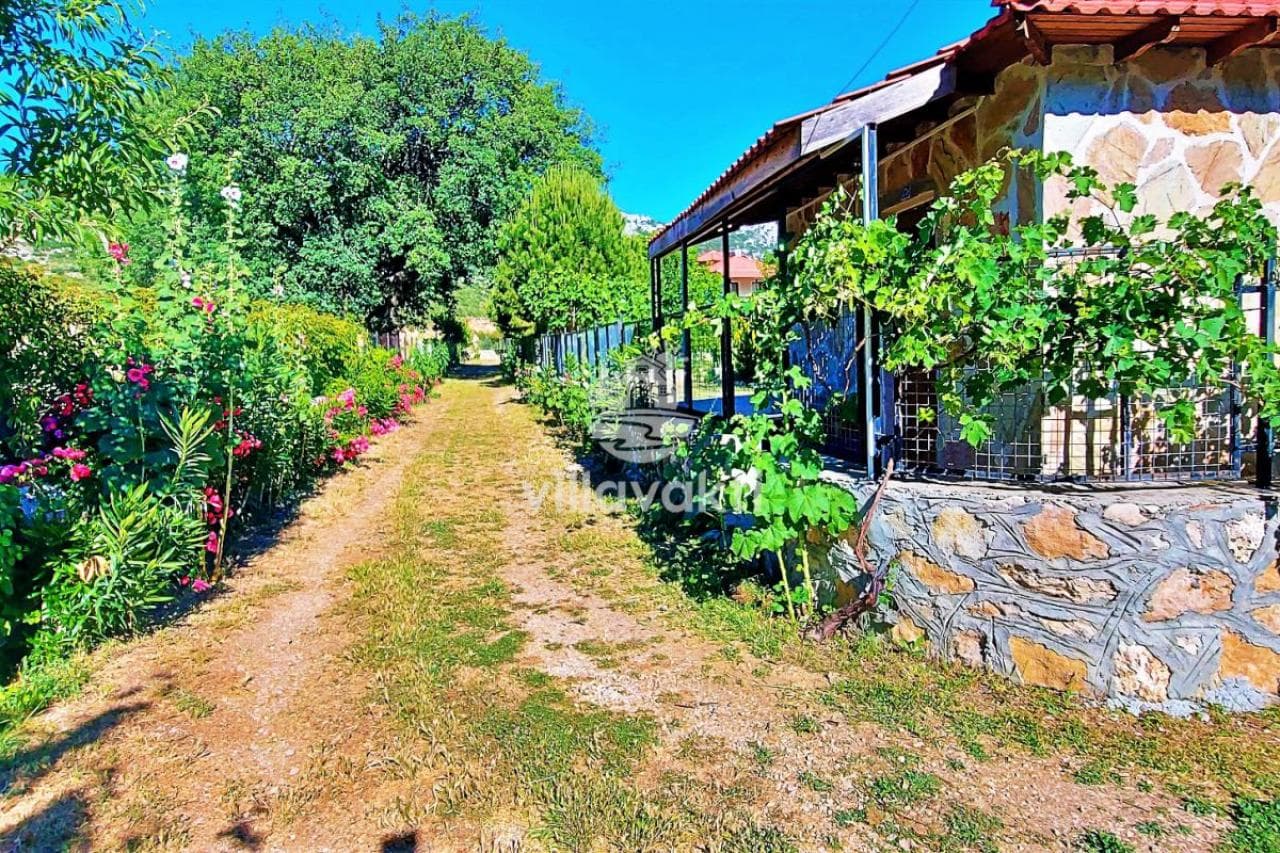 Çiçekler ve yeşilliklerle çevrili toprak yol ve taş duvarlı yapı.