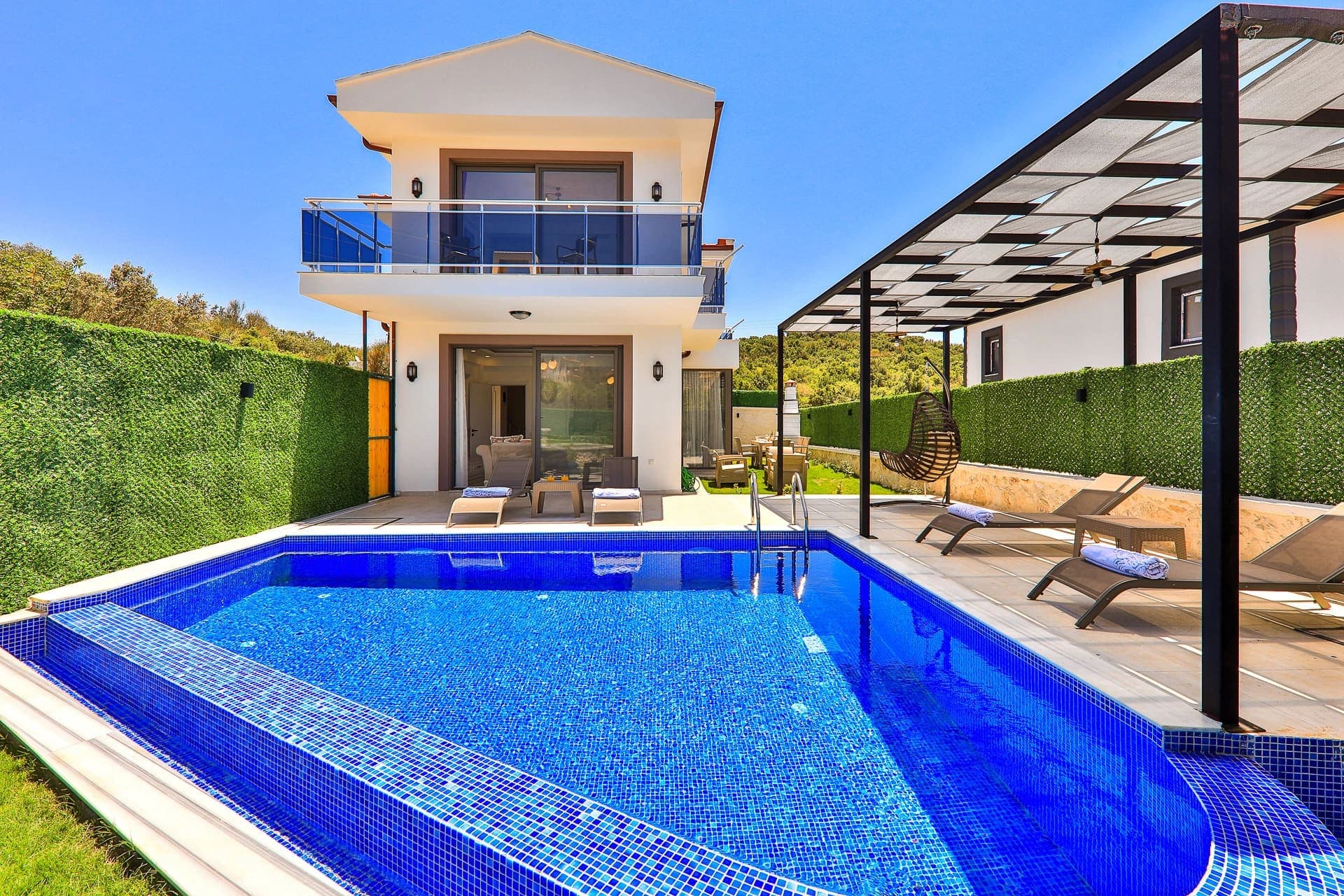 Önünde mavi havuz ve şezlonglar bulunan iki katlı modern beyaz villa.