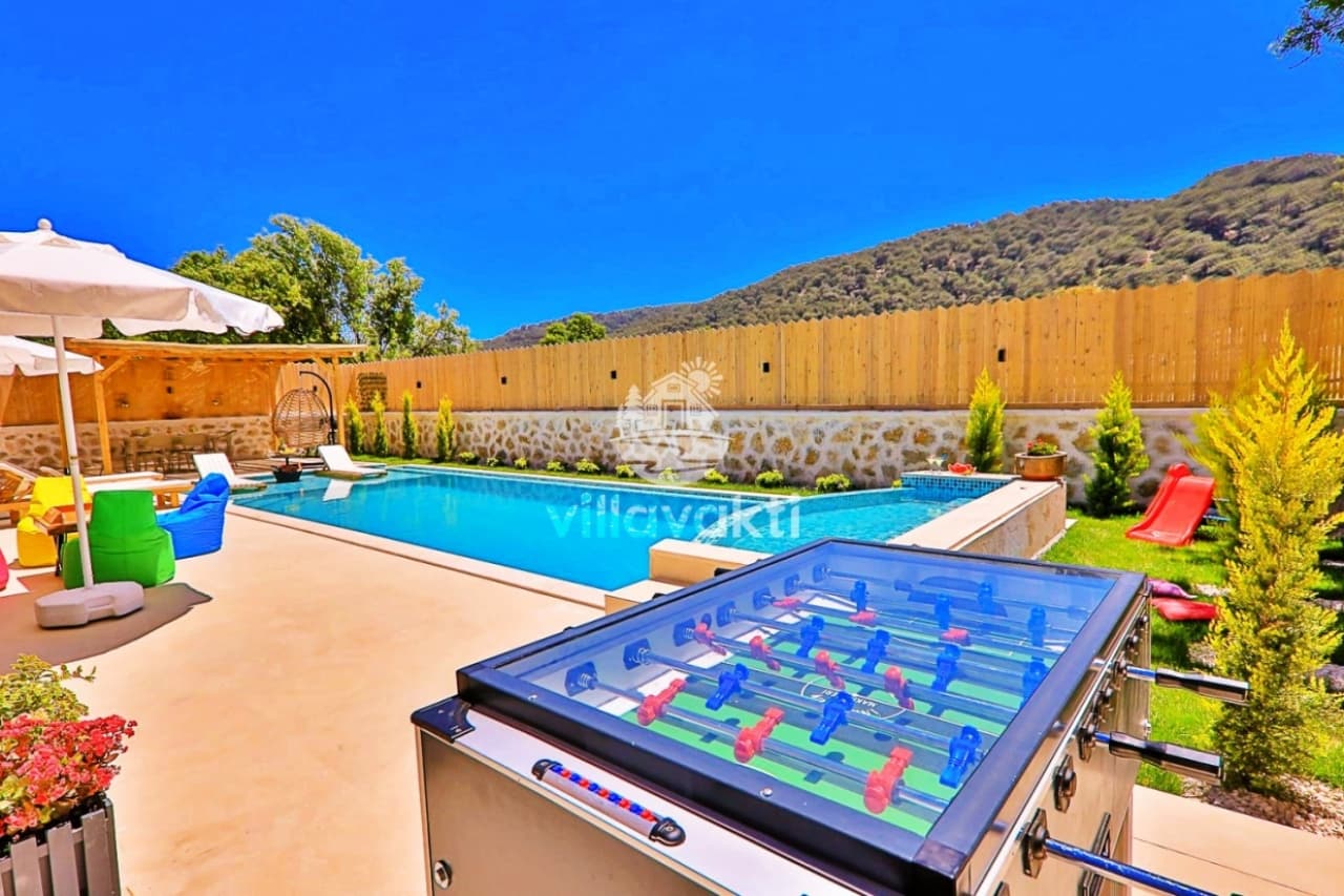 Açık havuz kenarında şezlonglar, masa tenisi ve dağ manzarası bulunan havuz alanı.