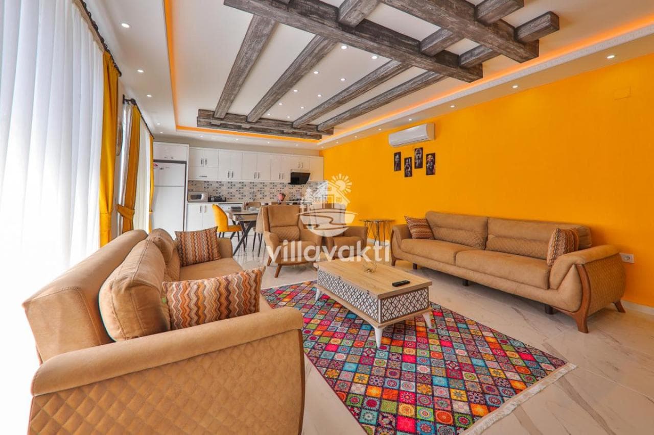 Sarı tonların hâkim olduğu, renkli halılı ve ahşap detaylı salon.