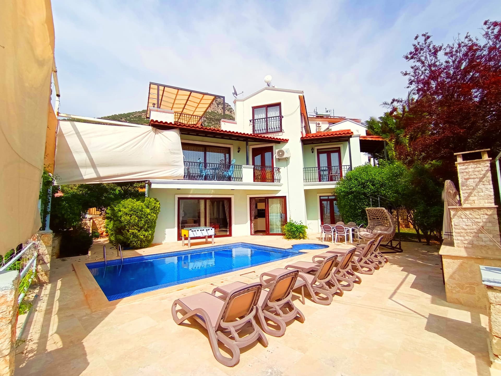 Havuz başında şezlonglar ve şemsiyeler bulunan çok katlı villa.