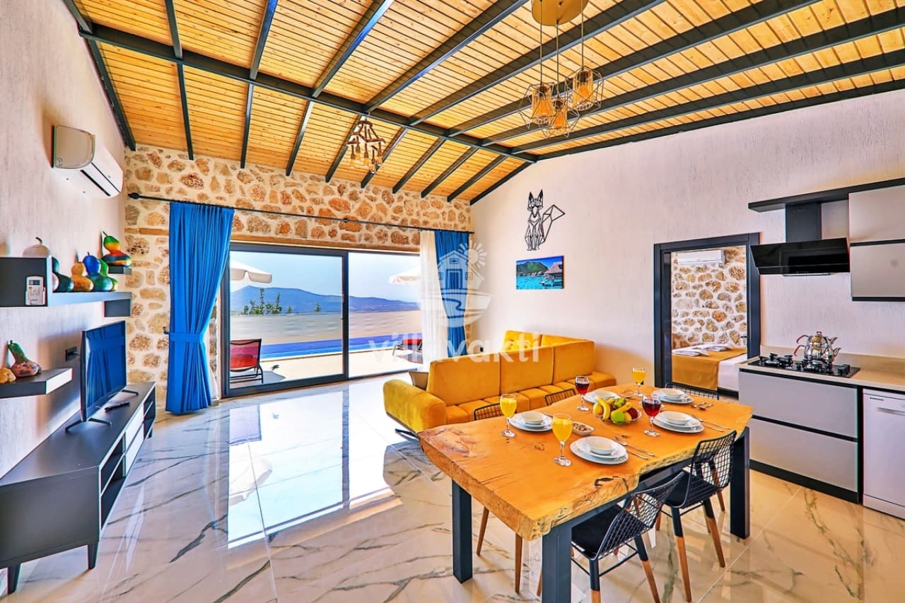 Ahşap tavanlı taş duvarlı salonda sarı koltuk ve yemek masası.