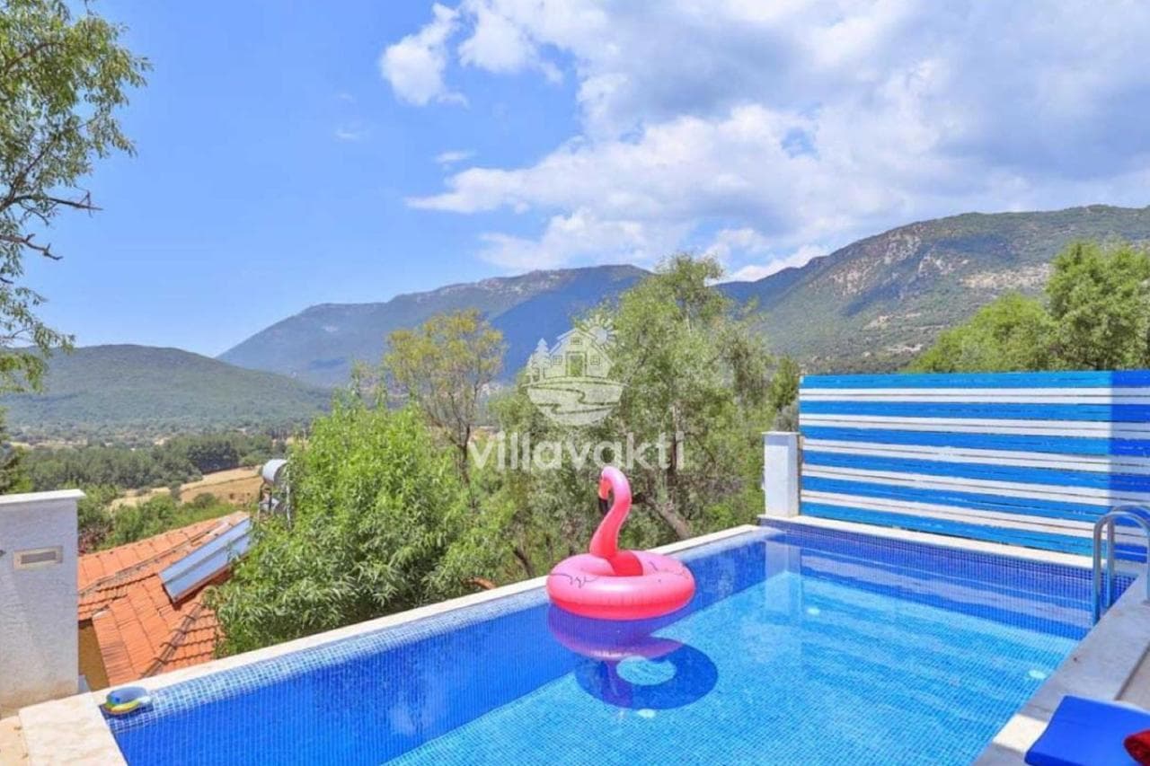 Dağ manzaralı açık havuz ve üzerinde pembe flamingo simidi.