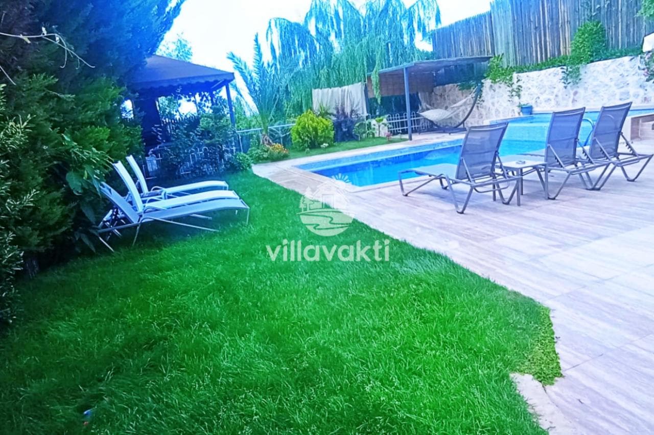 Yeşil çimler ve şezlongların bulunduğu villanın havuzlu bahçesi.