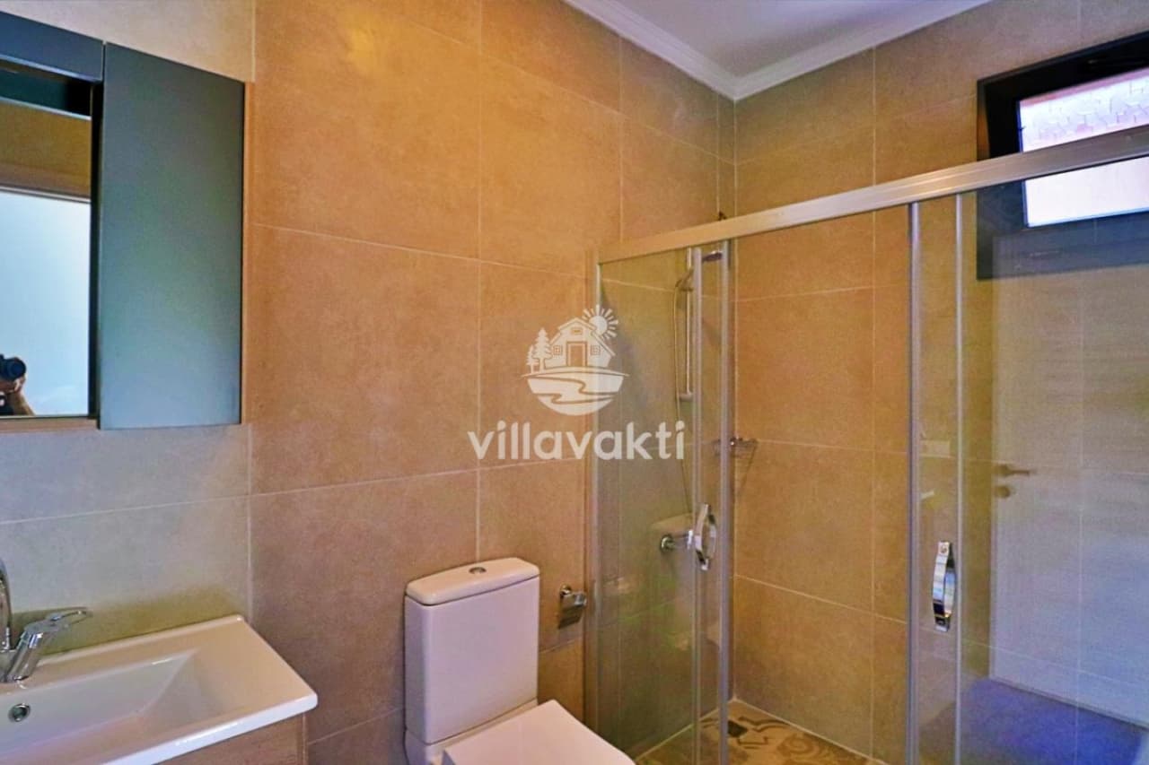 Bej seramik kaplı, cam duş kabinli ve lavabolu banyo.