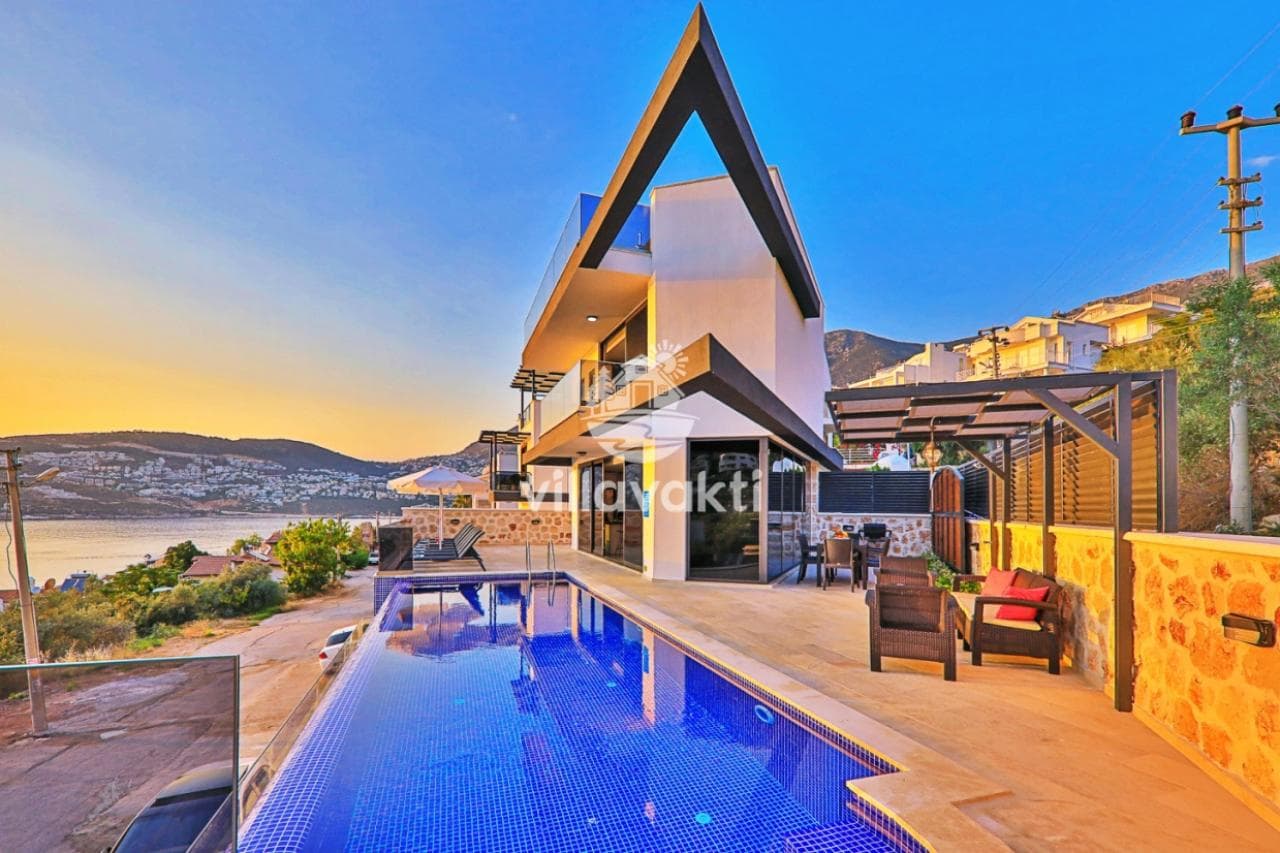 Gün batımında denize bakan havuzlu ve modern mimarili villanın dış cephesi.
