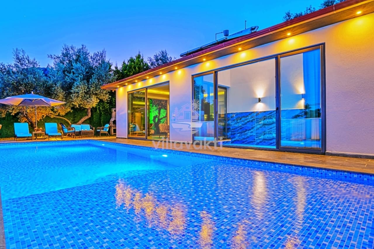 Akşam aydınlatmalı havuz kenarında şezlonglar bulunan villa cephesi.