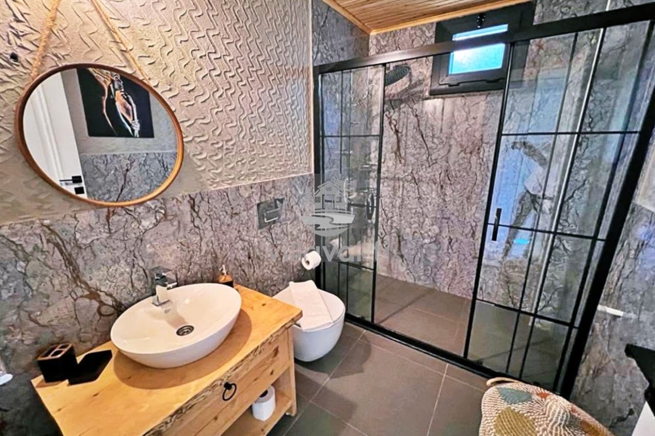 Mermer detaylı banyoda ahşap tezgâhlı lavabo ve siyah çerçeveli duş.