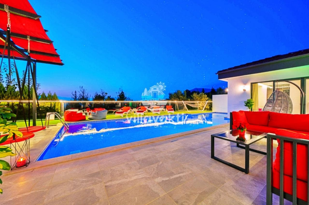 Açık havada havuz başı oturma grubu ve salıncak bulunan aydınlatmalı villa bahçesi.