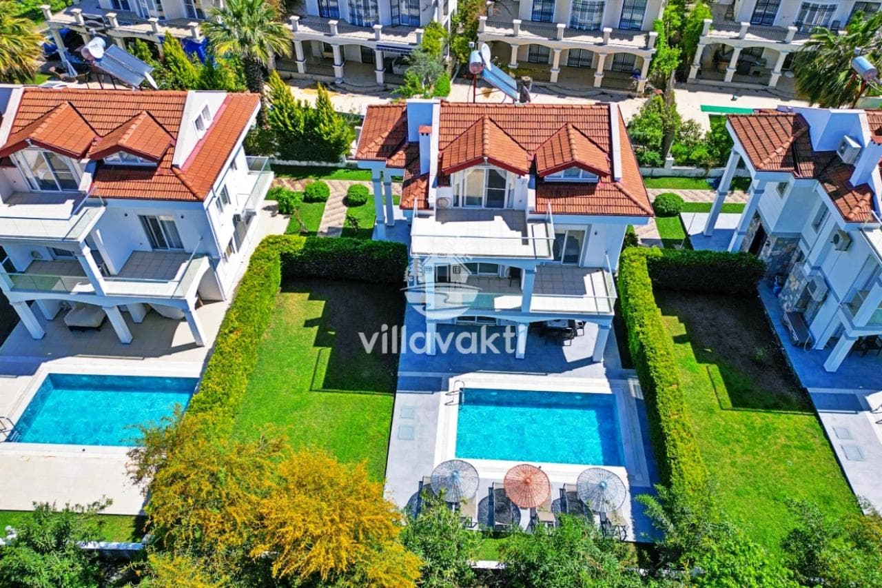 Yeşillikler içindeki ikiz villaların havuzları ve şezlongları havadan görünüm.