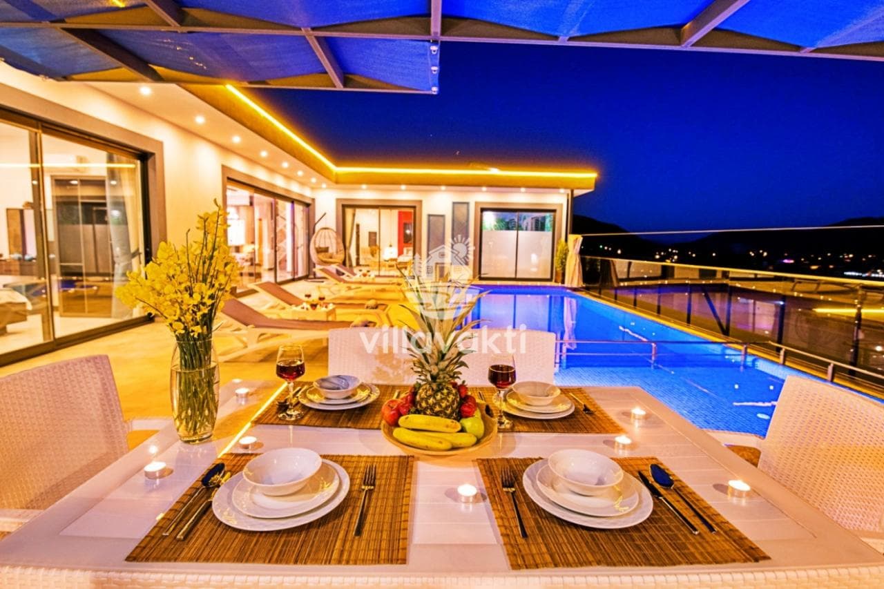 Özel havuz kenarında şık masa düzeni ve gece aydınlatmalı villa terası.