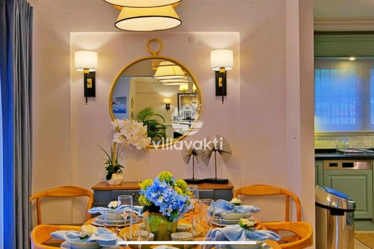 Mavi ve beyaz detaylarla süslenmiş yemek masası ve duvarda yuvarlak ayna.