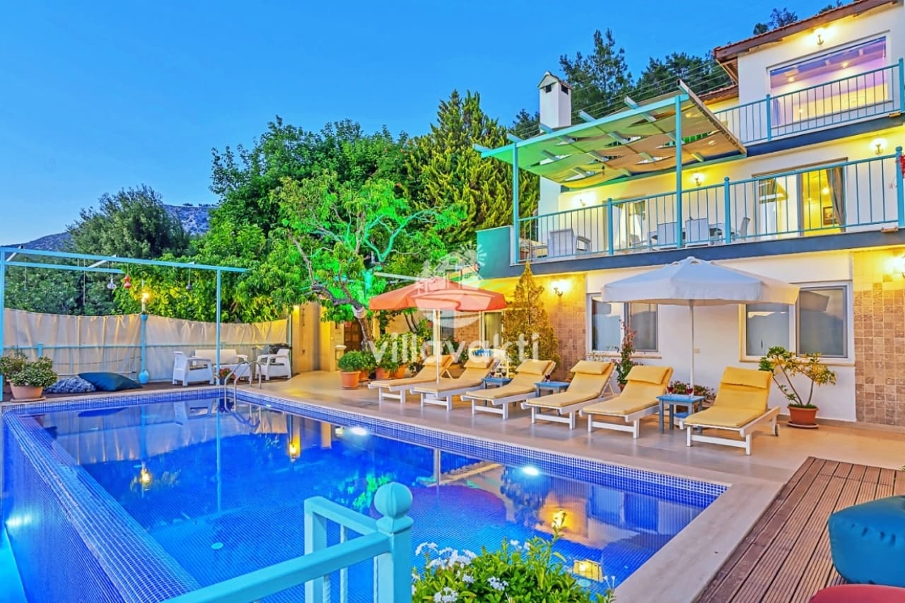 Akşam aydınlatmalı havuz kenarında şezlonglar ve arka planda villa dış cephesi.