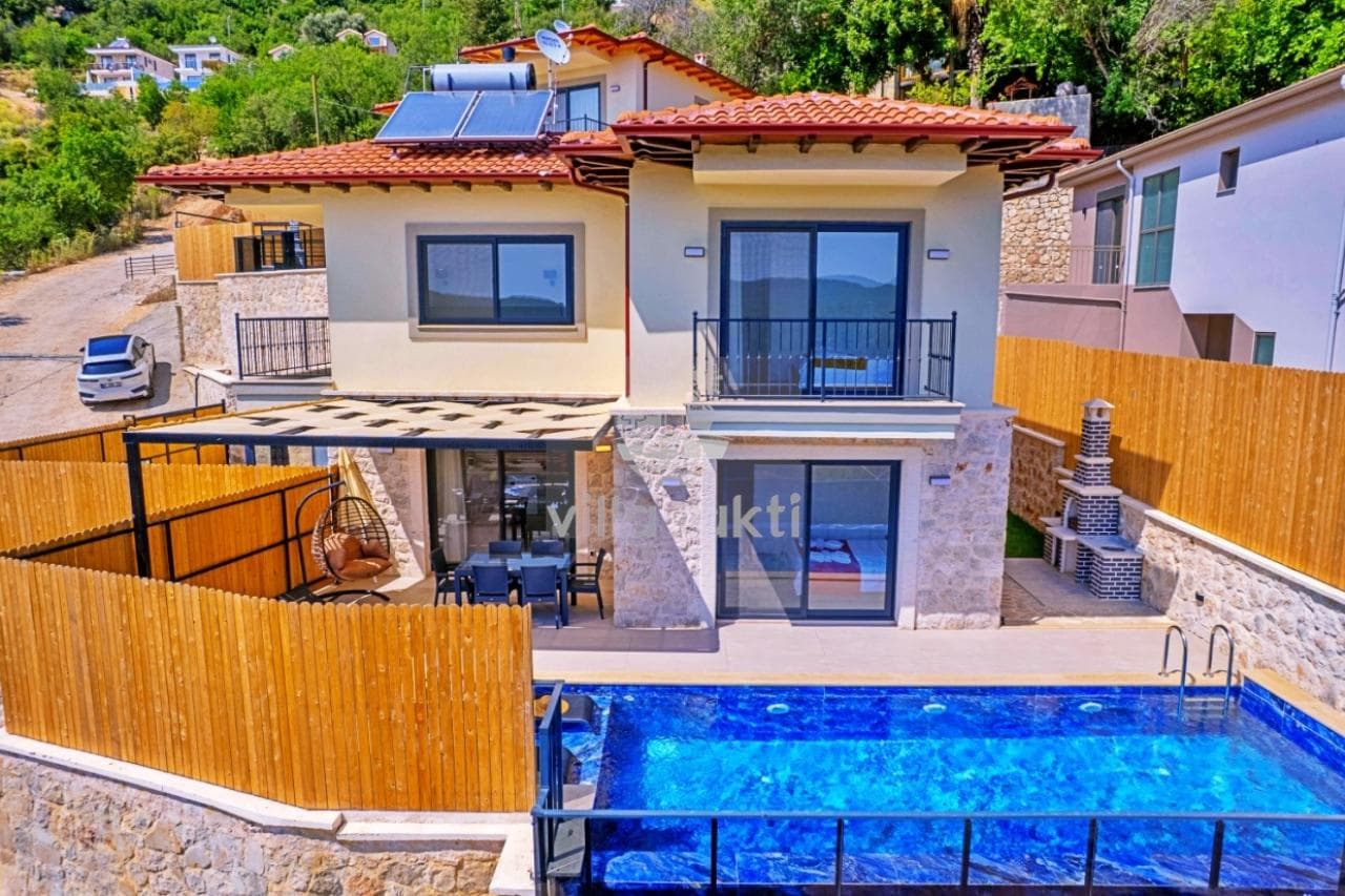 Önünde havuz, şezlonglar ve yemek masası bulunan, kiremit çatılı taş kaplama villa.