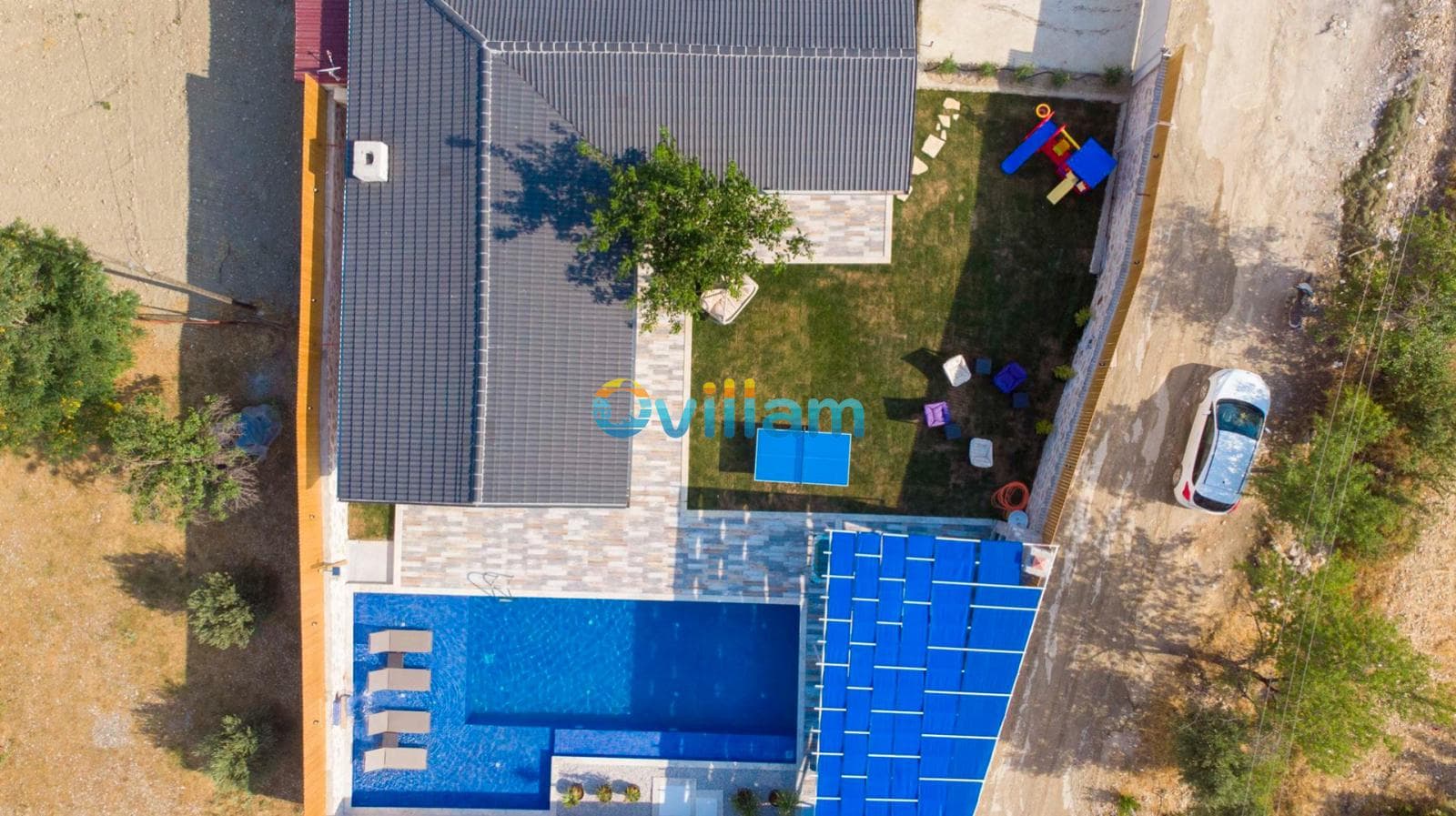Kuş bakışı görünümde bahçeli villa, yüzme havuzu ve çocuk oyun alanı.