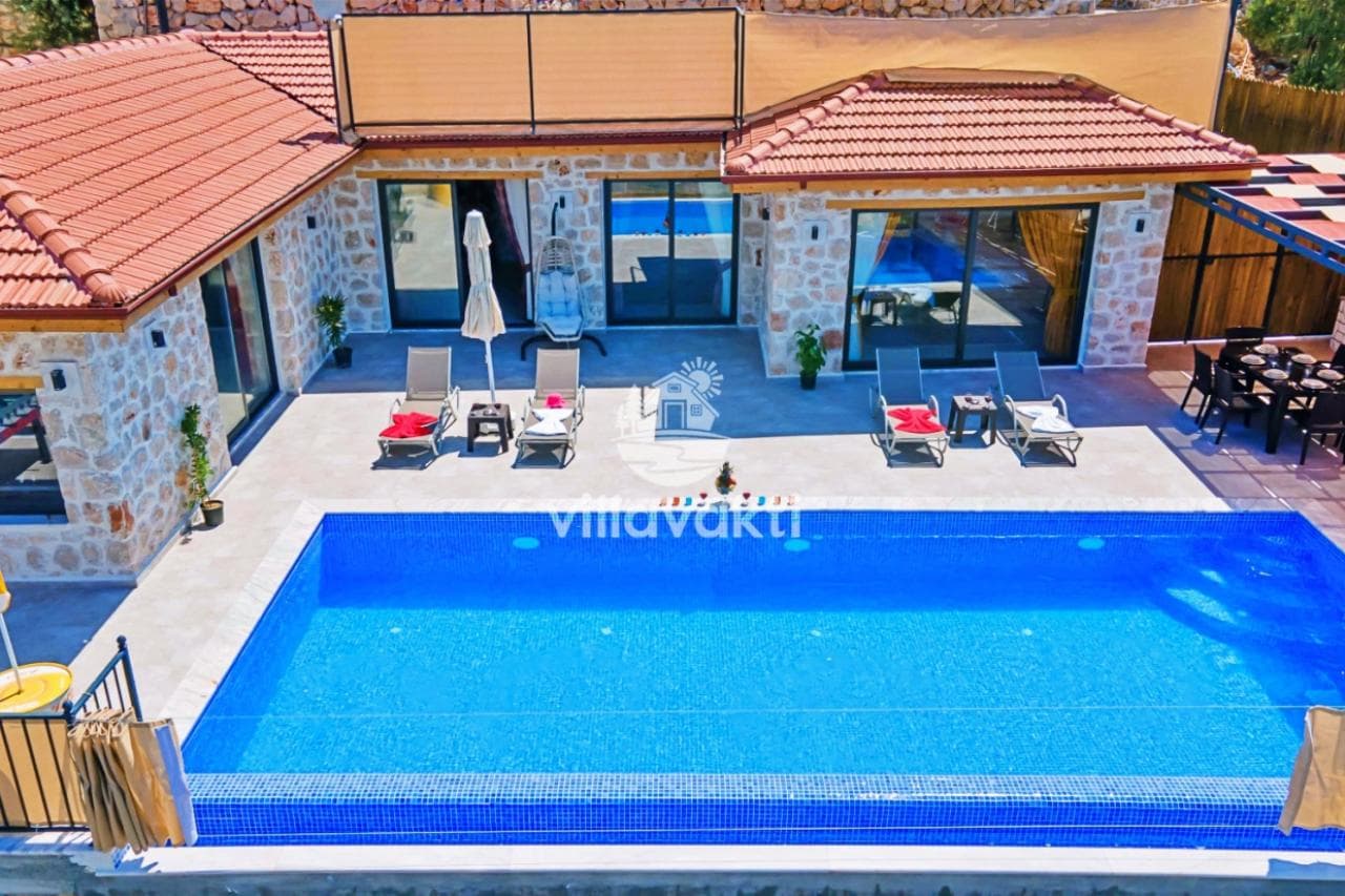 Taş duvarlı, havuz başında şezlongları ve yemek alanı bulunan villa dış cephesi.